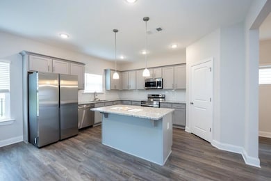 Kitchen featuring visible vents, a center island, hanging light fixtures, light stone countertops, and stainless steel appliances