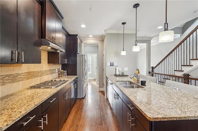 Kitchen featuring appliances with stainless steel finishes, under cabinet range hood, ornamental molding, dark wood-style flooring, and light stone counters