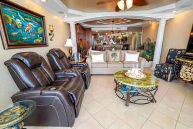 Living room featuring decorative columns, crown molding, light tile patterned floors, a chandelier, and ceiling fan