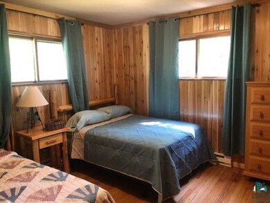 Bedroom featuring wooden walls, multiple windows, and wood finished floors