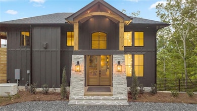 View of front facade with board and batten siding, a shingled roof, and stone siding