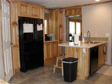 Kitchen with dark tile floors, light stone countertops, light brown cabinets, black appliances, and sink