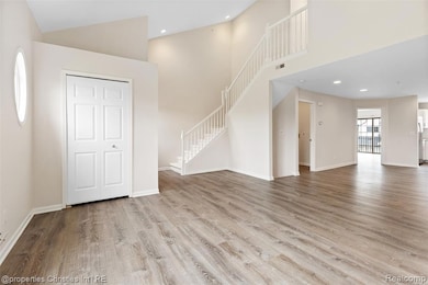Unfurnished living room with high vaulted ceiling, light wood-style floors, recessed lighting, and stairway
