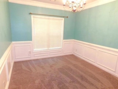 Carpeted empty room featuring crown molding, a decorative wall, a chandelier, and wainscoting