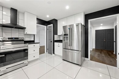 Kitchen featuring appliances with stainless steel finishes, wall chimney range hood, white cabinetry, dark countertops, and recessed lighting