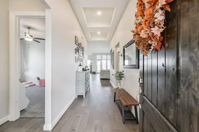 Bright hallway with wood flooring, tray ceilings, and recessed lighting. Sightlines to the living area create an open and airy feel.