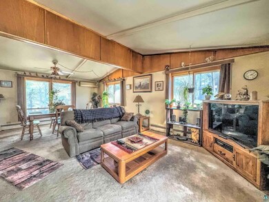 Carpeted living area featuring a baseboard heating unit, plenty of natural light, vaulted ceiling with beams, and ceiling fan