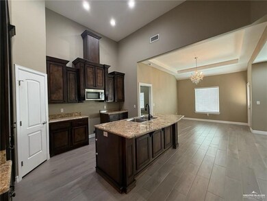 Kitchen featuring a chandelier, light wood-style flooring, dark brown cabinets, a center island with sink, and a tray ceiling