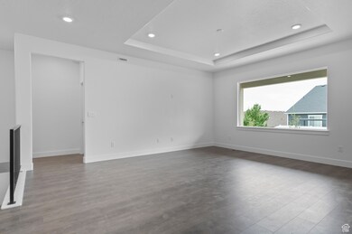Empty room with a tray ceiling, dark wood-type flooring, and recessed lighting