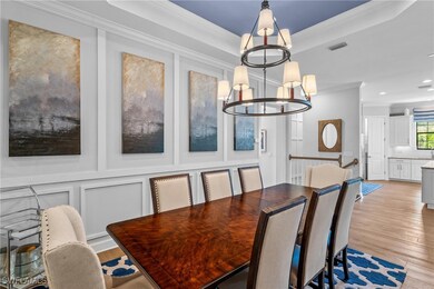 Dining space with ornamental molding, a raised ceiling, light wood finished floors, a chandelier, and a decorative wall