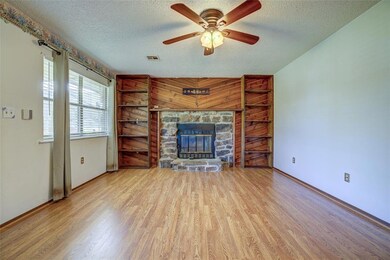 Unfurnished living room featuring a textured ceiling, wood finished floors, baseboards, a ceiling fan, and a stone fireplace