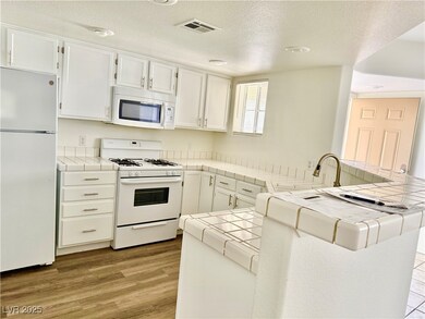 Kitchen featuring tile counters, white appliances, light wood finished floors, white cabinets, and a textured ceiling