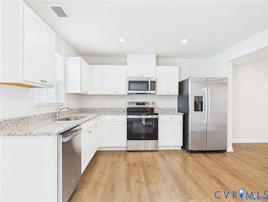 Kitchen with stainless steel appliances, light wood finished floors, white cabinets, light stone counters, and recessed lighting