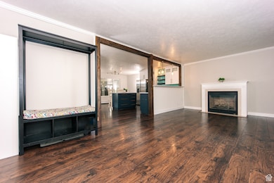 Current - Unfurnished living room with ornamental molding, dark wood-style flooring, a textured ceiling, and a fireplace with flush hearth