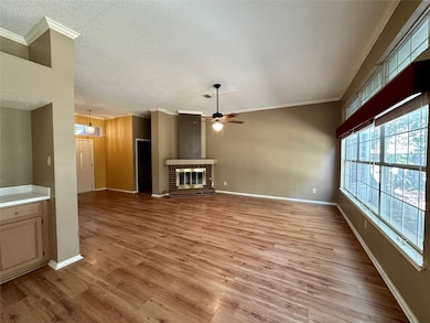 Unfurnished living room featuring ornamental molding, light wood-style flooring, ceiling fan, a fireplace, and a textured ceiling