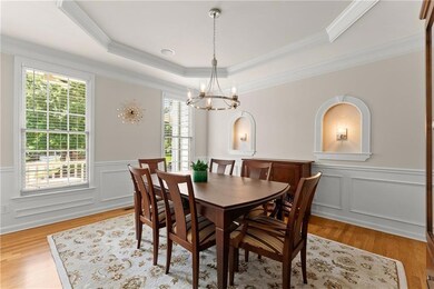 Dining area featuring a raised ceiling, a chandelier, crown molding, light wood-style flooring, and wainscoting