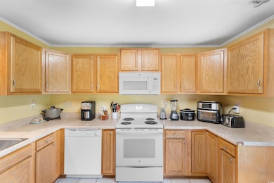 Kitchen featuring white appliances, light countertops, light tile patterned floors, and light brown cabinets