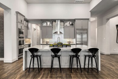 The heart of the home, this gourmet kitchen presents a striking front view defined by modern design. A prominent stainless steel vent hood is the focal point above the cooktop, complemented by a stylish, contemporary tile backsplash. Enjoy expansive and ample storage solutions thanks to the custom, full-height cabinets.