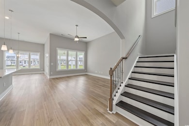 Unfurnished living room with ceiling fan, light wood-style flooring, arched walkways, a chandelier, and stairs