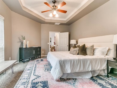 Carpeted bedroom with a tray ceiling, crown molding, and a ceiling fan