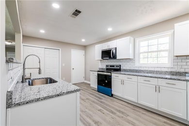 Kitchen featuring stainless steel range with electric stovetop, light wood-style flooring, tasteful backsplash, white cabinetry, and a sink