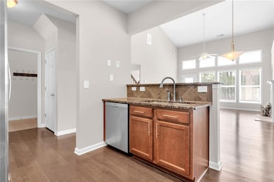 Kitchen featuring brown cabinetry, dark stone countertops, hanging light fixtures, a peninsula, and dark wood-style floors