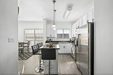 This photo showcases a modern kitchen with white cabinets, stainless steel appliances, and a breakfast bar. The space is bright and open, with natural light from large windows. The kitchen flows into the open concept living area.