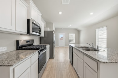 Kitchen with appliances with stainless steel finishes, a kitchen island with sink, white cabinets, recessed lighting, and light stone countertops