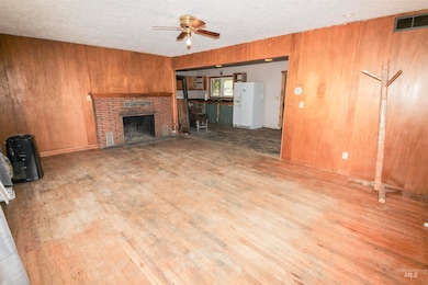 Unfurnished living room featuring wooden walls, ceiling fan, a textured ceiling, a fireplace, and wood finished floors