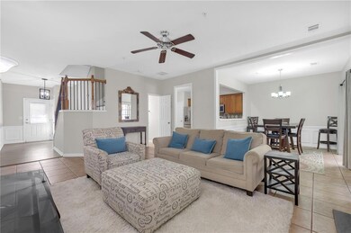 Living area featuring a chandelier, light tile patterned floors, ceiling fan, a wainscoted wall, and a decorative wall