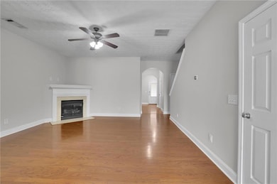 Unfurnished living room featuring light wood-style flooring, arched walkways, a fireplace with flush hearth, a textured ceiling, and a ceiling fan