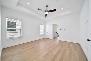 This bright, modern Master Bedroom with white walls, and recessed lighting. It includes a sleek ceiling fan, windows with blinds, and a doorway leading to a staircase.