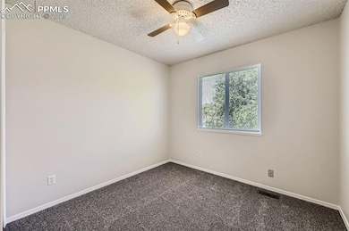 Unfurnished room with a textured ceiling, dark colored carpet, a ceiling fan, and baseboards