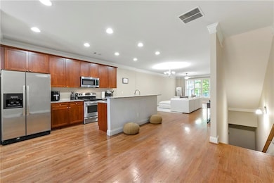 Kitchen with stainless steel appliances, ornamental molding, open floor plan, light wood-type flooring, and light countertops