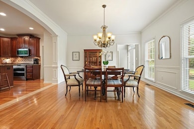 Dining area featuring light wood-style flooring, arched walkways, crown molding, a chandelier, and a decorative wall