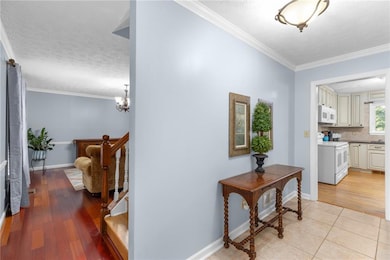 Corridor with ornamental molding, a textured ceiling, light wood-style flooring, and a chandelier