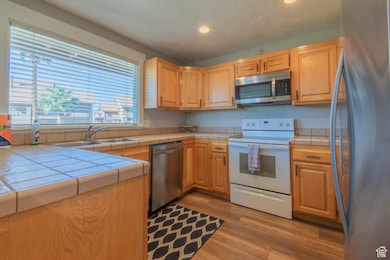 Kitchen featuring stainless steel appliances, tile counters, light wood-style floors, and recessed lighting