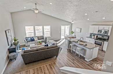 Living room with wood finished floors, ceiling fan, vaulted ceiling, a textured ceiling, and recessed lighting