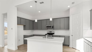 Kitchen with gray cabinets, a kitchen island with sink, decorative backsplash, pendant lighting, and light wood finished floors