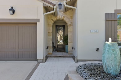 This entrance features a charming stone archway leading to a front door with decorative glass.  Entryway is accented by a modern water feature and sleek outdoor lighting, offering a welcoming and elegant ambiance.
