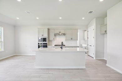 Kitchen with backsplash, recessed lighting, a center island with sink, black oven, and light stone counters