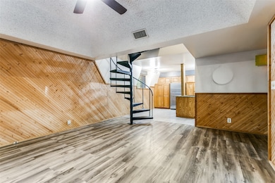 Unfurnished living room with wooden walls, stairs, wood finished floors, wainscoting, and a textured ceiling