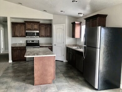 Kitchen with stainless steel appliances, vaulted ceiling, dark brown cabinets, dark tile patterned floors, and a textured ceiling