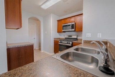 Kitchen featuring appliances with stainless steel finishes, arched walkways, brown cabinetry, light countertops, and light tile patterned floors