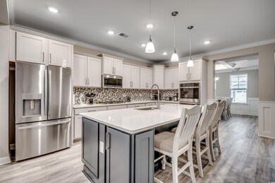 Kitchen featuring stainless steel appliances, crown molding, light countertops, light wood-style floors, and decorative backsplash