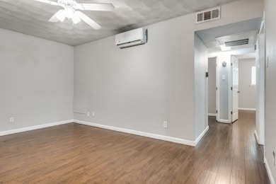 Unfurnished room with an AC wall unit, a ceiling fan, and wood finished floors