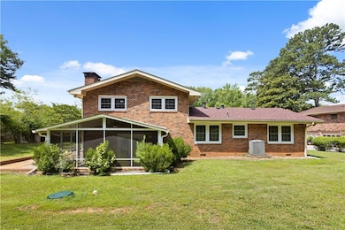 Rear view of property featuring a chimney, crawl space, a lawn, a sunroom, and brick siding