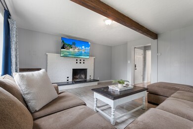 Living room featuring wood walls, wood finished floors, a brick fireplace, and beam ceiling