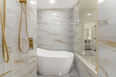 Full bathroom featuring stone wall, a soaking tub, tile walls, recessed lighting, and marble tiled flooring