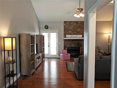 Living room featuring ceiling fan, dark wood-type flooring, and a stone fireplace